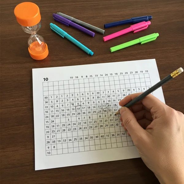 Hand filling in a blank multiplication chart with a pencil